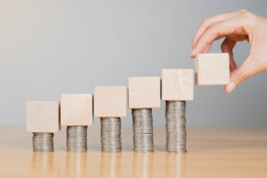 İnsan eli, beyaz arka plandaki bozuk para yığını üzerinde tahta bloklar tutuyor iş sermayesini artırıyor, daha fazla yatırım yapıyor. Fon yatırım kavramı