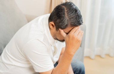 Evde oturan olgun bir adamın yüksek açılı görüntüsü, kapıya yakın, eli kafasında. Stres ve baş ağrısı.