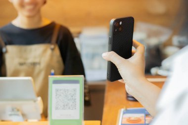 Dijital ödeme yöntemi kullanan kadın müşteri, bir kafede akıllı telefon ile QR kodunu tarayıp kredi kartı veya banka kartı kullanarak ödeme olarak para gönderiyor.