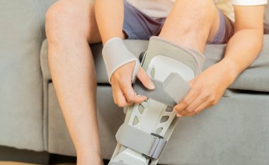 Evdeki kanepede oturan adamın ayak bileği ortozu. Ayak bileği ortozu. Boşluğu kopyala ve seçici odak.