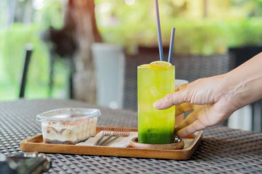 Bir insanın elinde taze limonla serpiştirilmiş taze yeşil çay, masada servis edilen şeffaf plastik bir pasta bulunur. Seçici odak.