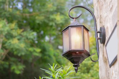 Doğa arka planında klasik tarzda asılı duran bir fener. Dökme demir, dekoratif cam paneller, sıcak ışık. Seçici odak.