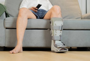 Evde geçirdiği trafik kazasından sonra elinde uzaktan kumandayla rahatlayan bir adamın görüntüsü. Yaralı bir adam televizyon izliyor.