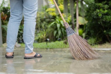 Bahçe yolunda yerleri süpürürken doğal sert süpürgesi olan bir kadının yan görüntüsü. Geleneksel bir hasır süpürge..