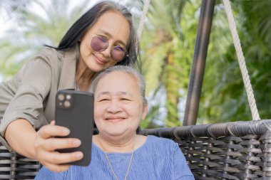 İki güzel komik Asyalı kadın mutlu anne ve kız tatilde akıllı telefonda ortak bir selfie çekiyorlar..