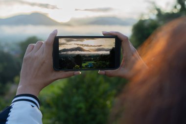 Kuzey Tayland 'daki yüksek dağlarda bir kadın telefon kamerasından fotoğraf çekiyor. Yüksek dağların önünde akıllı bir telefonla fotoğraf çeken bir kadın..