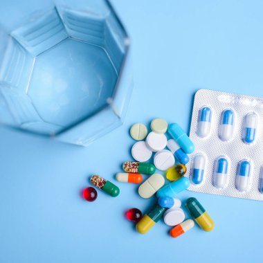 Haplar, tabletler, vitaminler ve açık mavi arka planda bir bardak su. Hap alma kavramı
