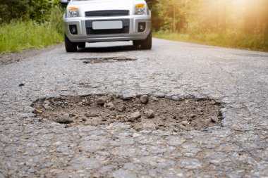 Otoyolda giden ve derin bir çukura yaklaşan bir SIIver arabası. Korkunç yol kavramı, yol tamir edilmeli.
