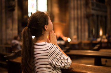 Dindar genç bir kadın Katolik kilisesinde bankta oturmuş dua ediyor, kilise yönetiminde yukarı bakıyor.