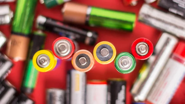 Background of batteries of different size and firm`s on a red background. Symbol of power. Ecological problem