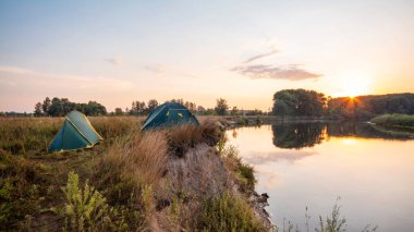 Nehrin kıyısında kamp yapmak. Sabah güneş doğarken nehrin yanında iki çadır.