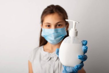 Koruyucu tıbbi maskeli kız sabunla şişeyi gösteriyor. Ellerini temiz tutma kavramı