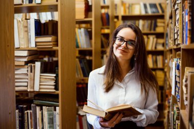 Kadın kütüphanede kitap okuyor.