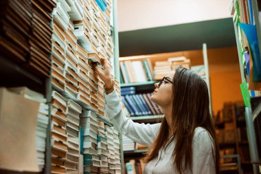 Okul çalışanı kitapları düzenliyor. Kütüphane çalışanı kitaplara ve kitaplara bakıyor.