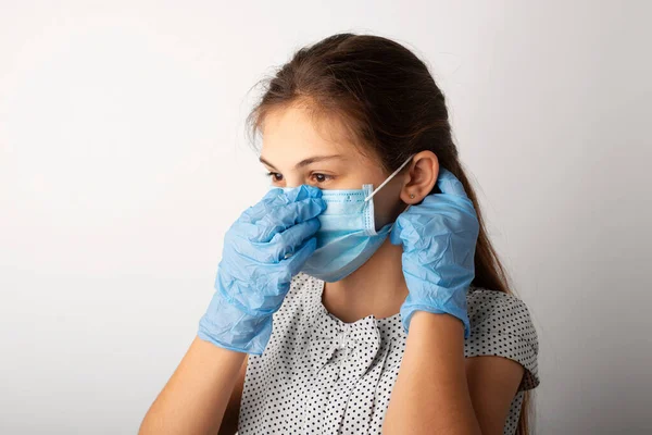 Small caucasian girl in medical mask and gloves in studio. School girl in dress puts on a protective medical mask