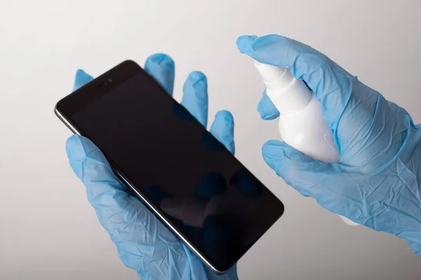 Hands in blue gloves applying sanitizing spray to a mobile phone to kill all the germs and keep device clean