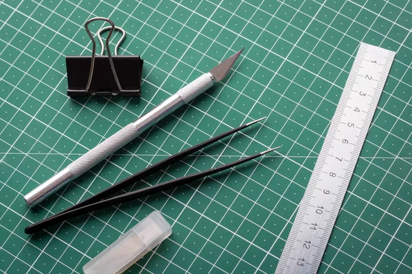 Stationery equipment on cutting mat. Scalpel, tweezers, and paper clip on the cutting mat before origami work