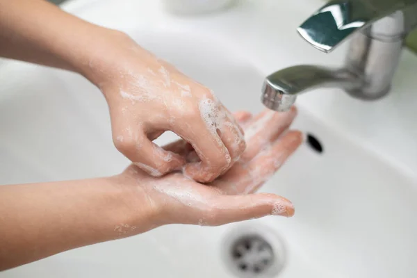 Self care and hygiene concept. Close-up shot of child`s hands while washing. Little girl carefully and slowely washes her hands with antibacterial soap to sanitize them