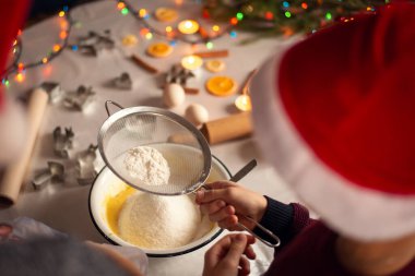 Kırmızı Noel Baba şapkalı küçük çocuk annesine bisküvi pişirmesinde yardım eder. Noel 'i kutlamak için hazırlık.