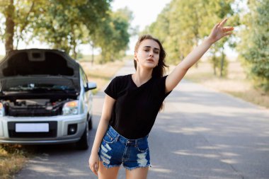 Kızın bozuk bir arabası var ve yardım istemek için yoldan geçen bir arabayı durdurmaya çalışıyor.