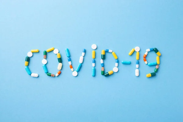 Inscription Covid-19 on blue medical background made of pills and capsules. Coronavirus concept