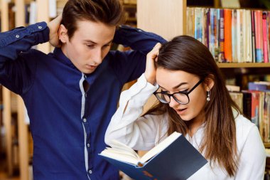 İki duygusal öğrenci kitabın içine bakıp başlarının yanında el ele tutuşuyorlar. Kütüphane, çalışma, bilgi arama.