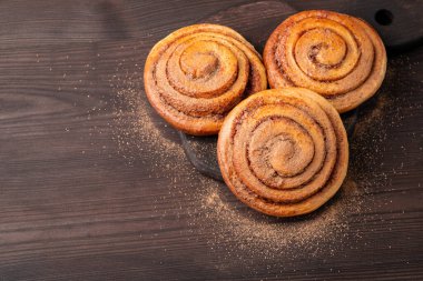 Koyu ahşap zemin üzerinde tarçınlı üç adet ekmekli çörek. Tarçın tozlu baharatlı ekmek