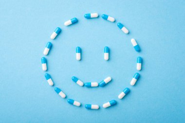 Mavi arka plandaki haplardan yapılmış olumlu bir gülümseme. İlaç, ilaç, tedavi, sağlık sigortası kavramı