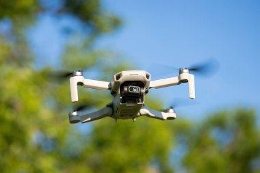 Arka planda ağaçlarla havada uçan küçük bir dron. Otonom uçan uçaklar video çekiyor ve fotoğraf çekiyor.