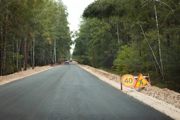 New asphalt road in the countryside and excavators making roadsides. New road construction