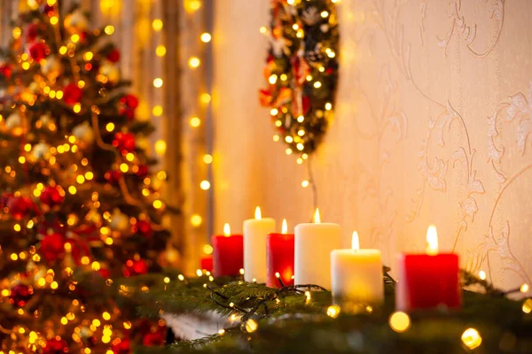 クリスマス用のキャンドルやライトで飾られた部屋 赤と白のろうそくを燃やし 壁に花輪 背景にクリスマスツリー — ストック写真