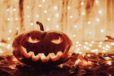Scary halloween pumpkin in the room lit by garlands. Creative cut pumpkin with spooky smile face