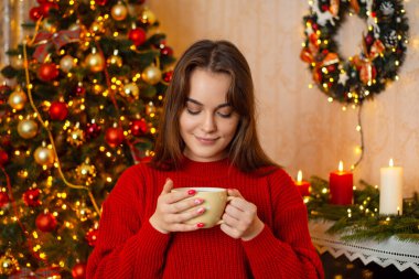 Sıcak kahve içen genç bir kadın ya da Noel ağacıyla sıcak bir odada dikilen kakao. Kış tatili havası, şenlikli atmosfer