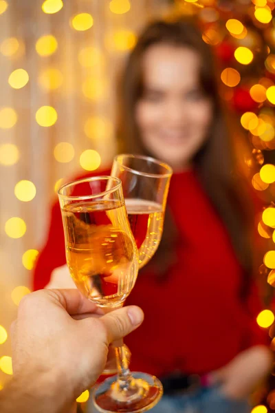 Two persons clink glasses full of champagne. New Years Eve, celebrating together with close friends and family, bright festive interior and mood