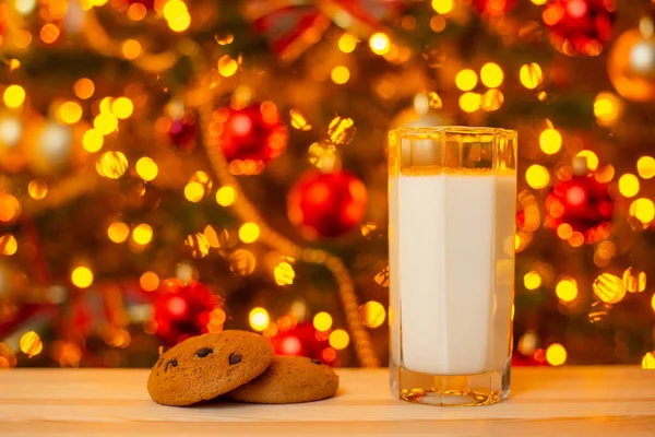 Glass of milk and some cookies on table on background of Christmas lights. Milk and snack for Santa concept