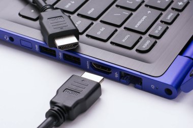 HDMI kablosunun iki ucu beyaz arka planda modern mavi dizüstü bilgisayarın HDMI portu yakınında.