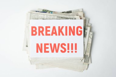 Üstünde kırmızı yazılar olan beyaz masanın üzerine yığılmış taze gazeteler.