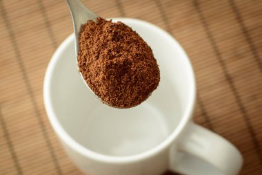 Sabahları sert kahve yapıyorum. Kahverengi arka planda beyaz fincanın yanında kaşık ve kahve.