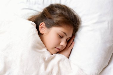 Küçük siyah saçlı kız geceleri güzel rüyalar görüyor. Yatakta rahat bir yastıkta uyuyor. Odasındaki sıcak beyaz battaniyeyle örtülü.