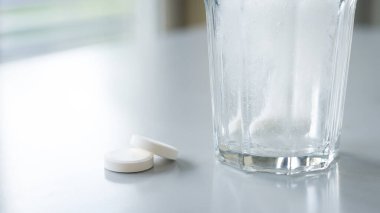 Çözünür tabletler. Bir bardak su ve beyaz masada çözünen haplar.