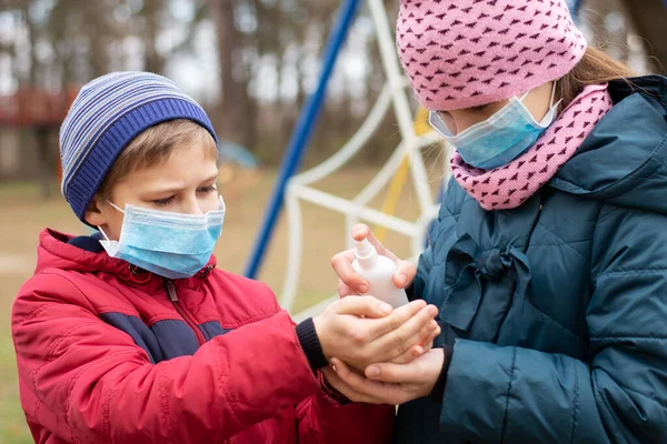 Girl applying cleaning gel on hands of a boy after playing on playground outdoor. Precautions while epidemic of dangerous virus