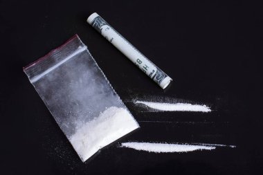 Plastik paketin yanındaki siyah masada iki sıra eroin ve uyuşturucu solumak için katlanan dolar banknotları.