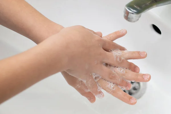 Girl washing hands in a correct way. Small child carefully washes hands with soap