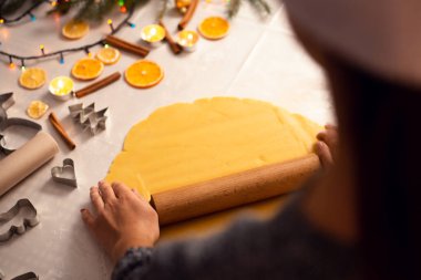 Dişi fırıncı kurabiye için hamur topluyor. Noel süslemeleri, yemek malzemeleri ve mutfak aksesuarlarıyla dolu bir masa..