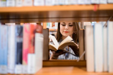 Kütüphane, raflarda bir sürü kitap, işe yarar bilgi bulmayı umarak kitabı karıştıran pozitif bir genç kız. Okuma, öğrenme ve zeka kavramı.