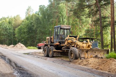 Old grader on the sideroad of new road. Machine for leveling the ground before asphalt road making in the countryside