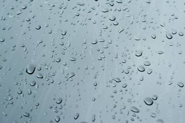 Rain drops on a window glass surface against a dark background of stormy sky.