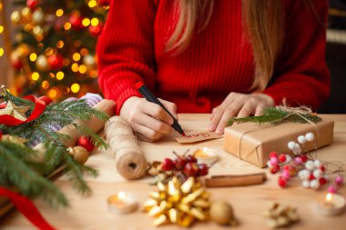 Decoration of Christmas presents on table full of decorations. Close up shot of girls hands, signing gift for a friend