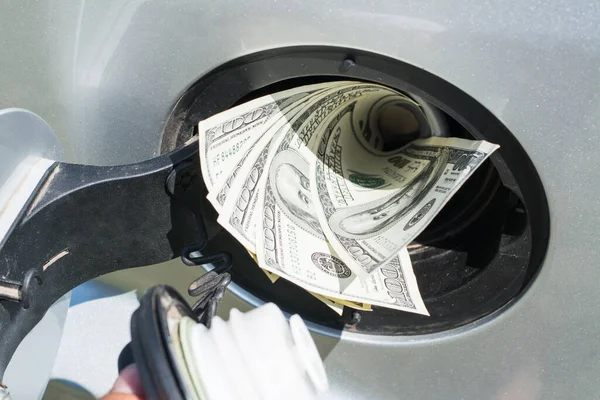 Fuel tank of a silver car filled with US dollar banknotes, symbolizing high cost of fuel