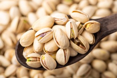 Dark wooden spoon with pistachios. Beautiful composition of pistachios. Tasty fresh salted nuts